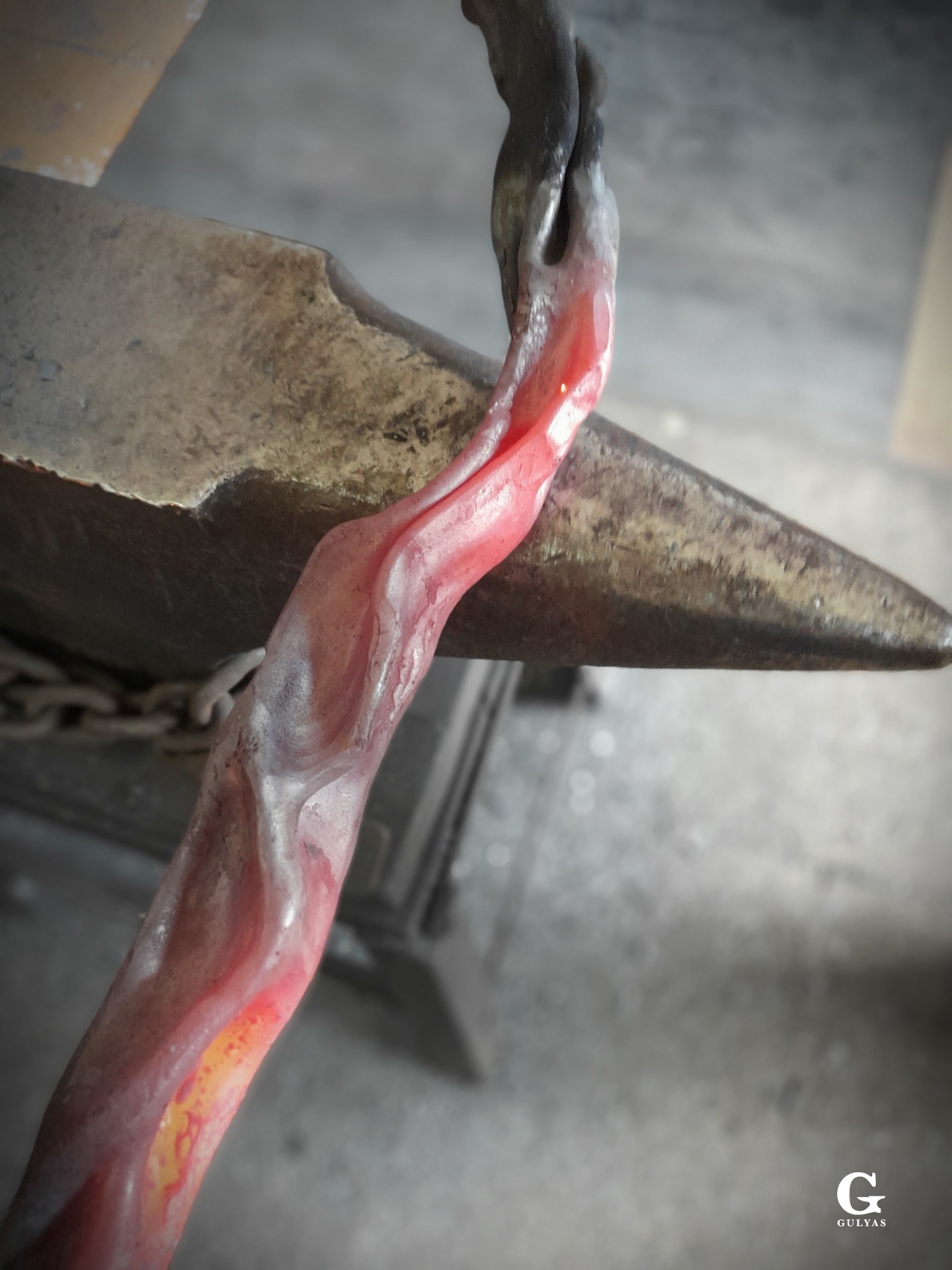 Top-down view of a finely forged, organically curved piece of metal resting on the anvil, its surface dark gray with a faint red glow still visible in places